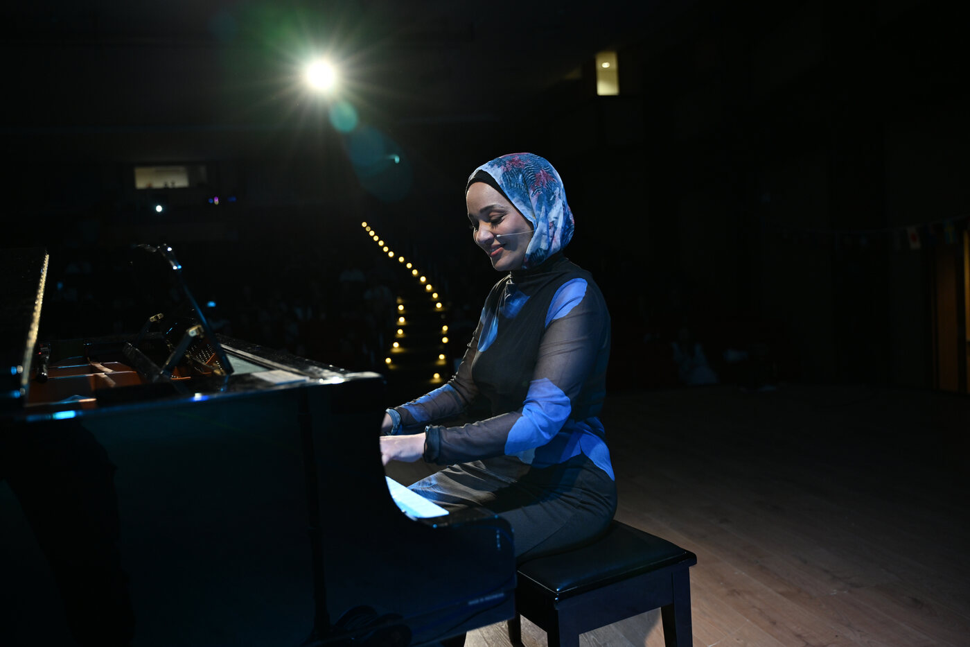 Yasmin Shennawy playing the piano under stage lighting